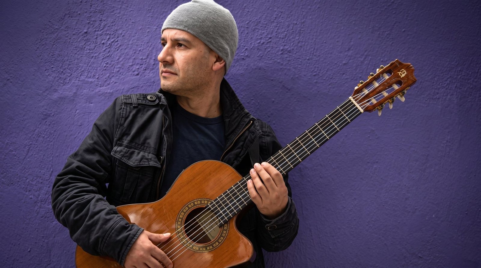 Alejandro Santiago con su guitarra acústica frente a un muro morado